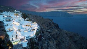 A coastal village with white buildings, a rocky coastline, and a view of the sea. - IKIES Santorini (Santorini)