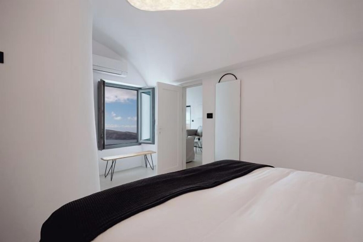 A modern bedroom with a large bed, a window with a view, and a desk with a chair.