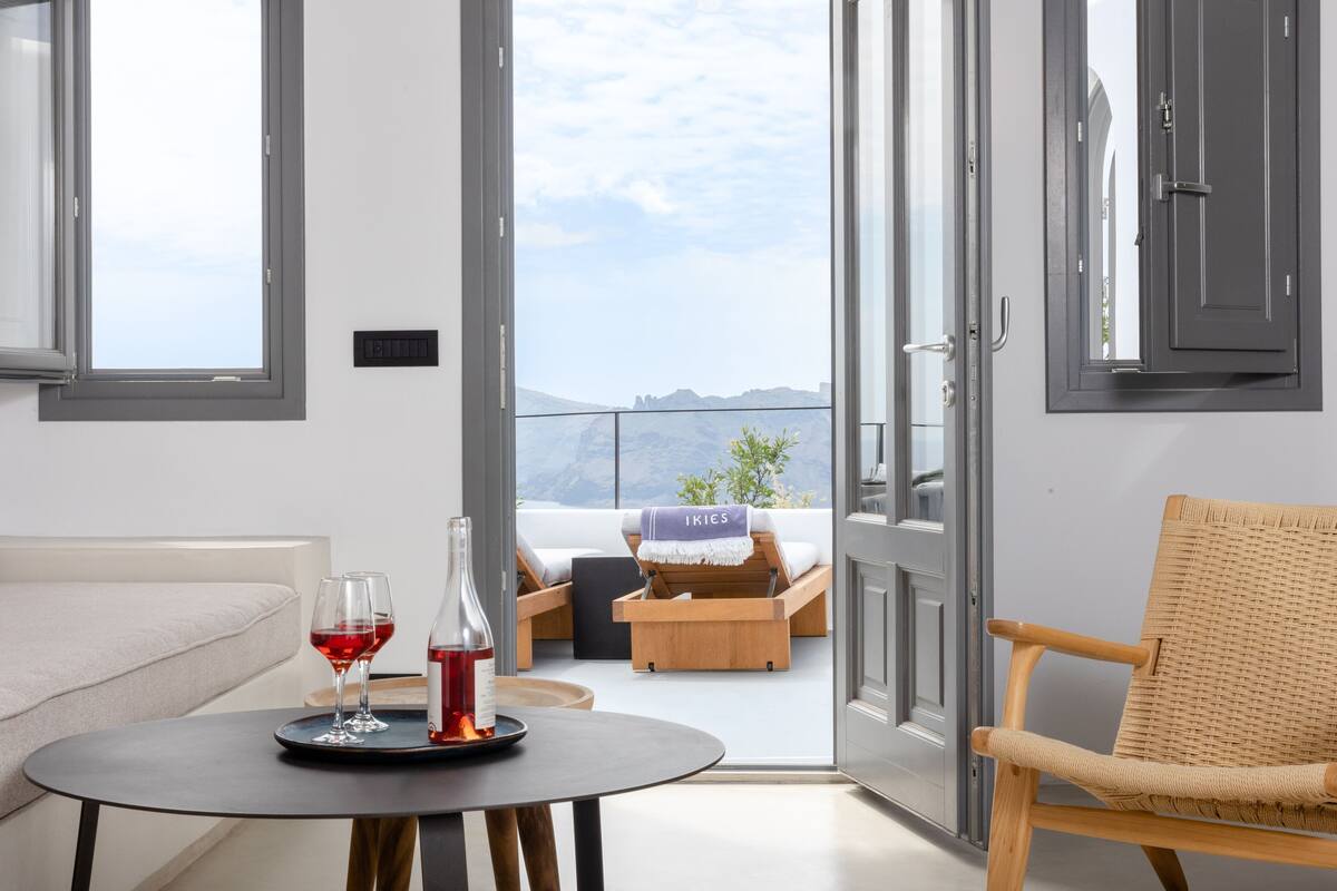 A modern room with a balcony, a sofa, a table with glasses and a bottle, and a wicker chair.