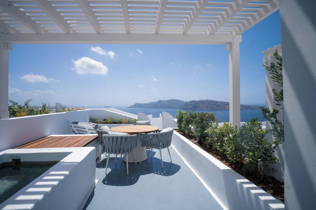 A terrace with a table and chairs, overlooking a scenic view of the sea and distant landforms.