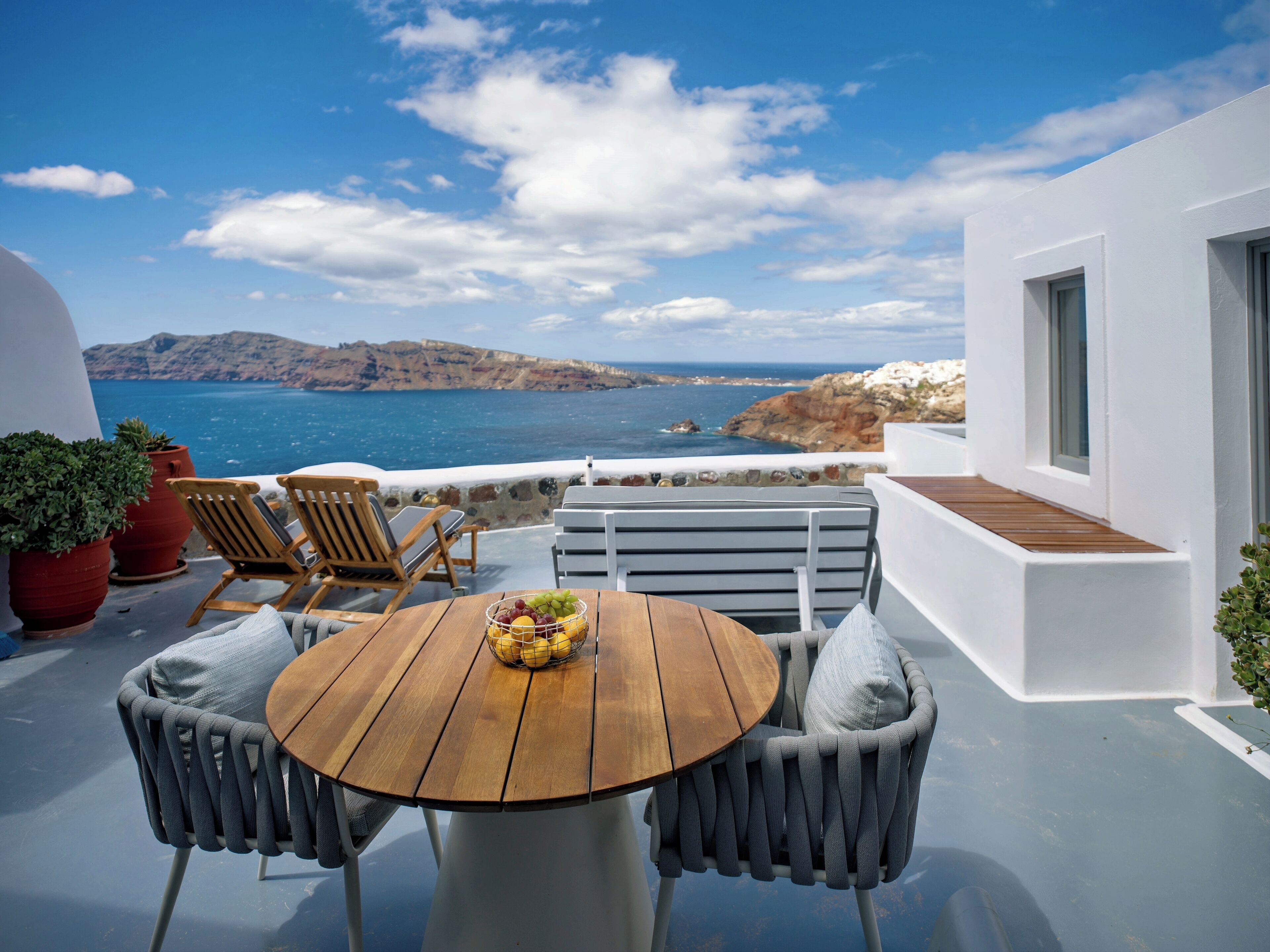 Una terraza con una mesa de madera y dos sillas, una planta en maceta y vistas al mar y a las montañas.