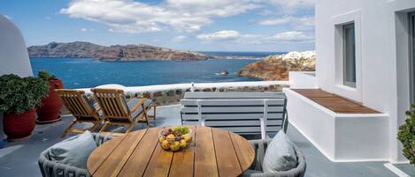 Una terraza con una mesa de madera y dos sillas, una planta en maceta y vistas al mar y a las montañas.