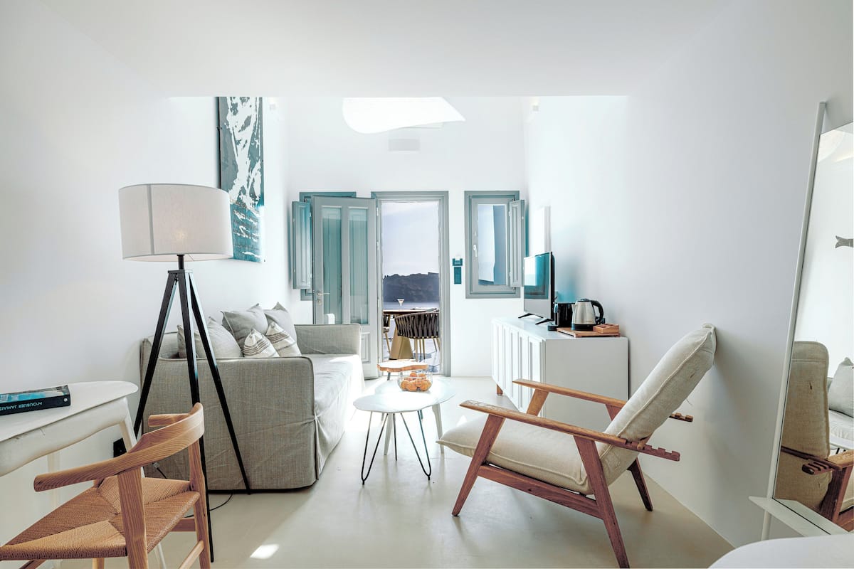A modern living room with a sofa, a coffee table, a lamp, and a chair. There is a view of the outdoors through the open door.