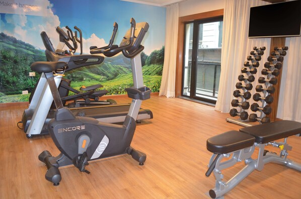 A gym with stationary bikes, a bench, and a wall-mounted dumbbell rack. - NH Buenos Aires Florida (Buenos Aires)