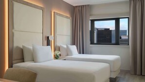 Habitación de hotel con dos camas, un escritorio y una ventana con cortinas.