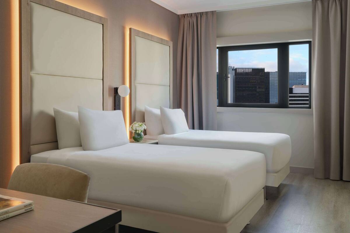 A hotel room with two beds, a desk, and a window with curtains.