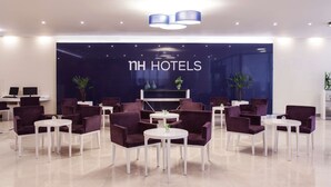 Un hall de hotel de diseño moderno, con sillas moradas y mesas blancas dispuestos en un espacio amplio.