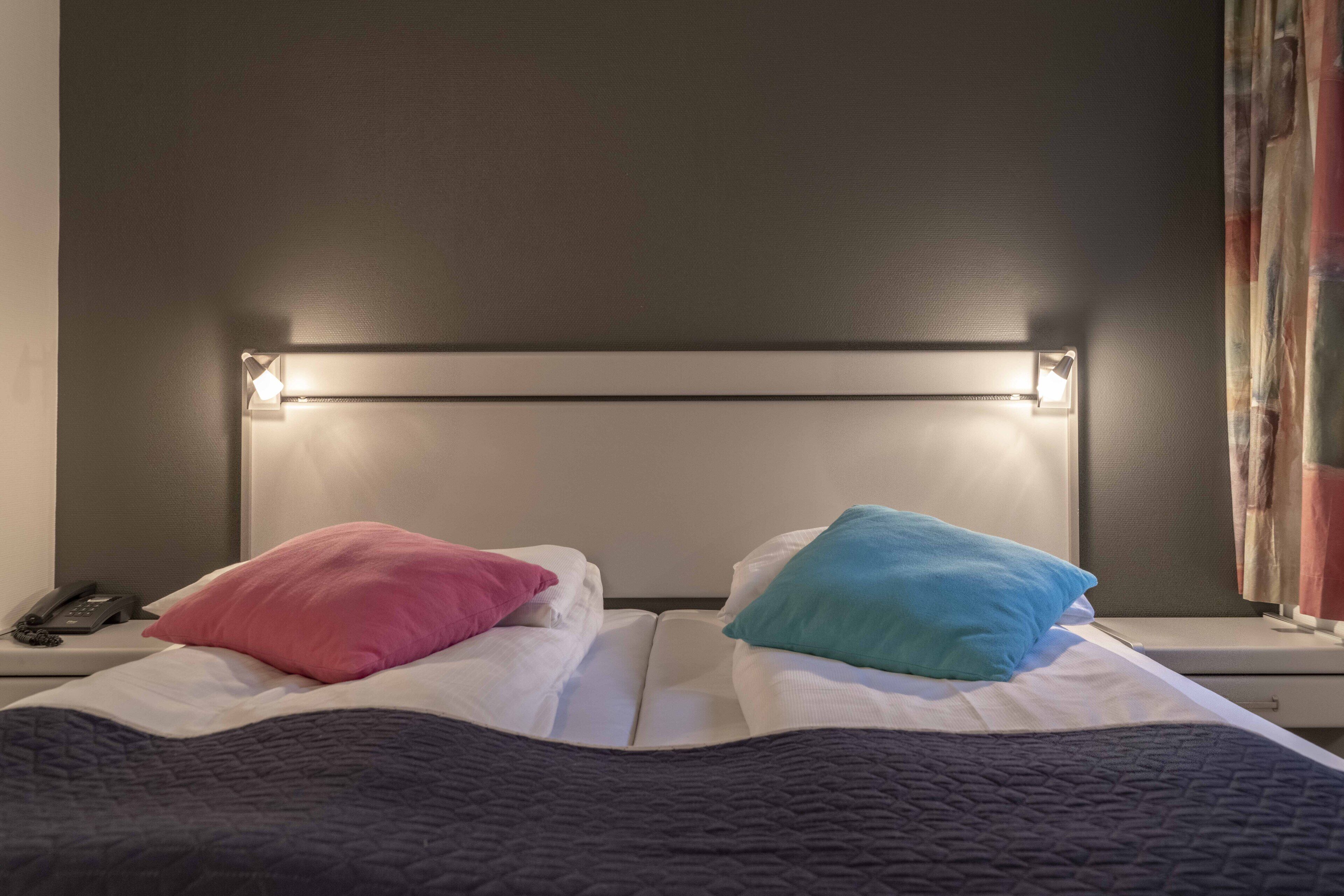 Una cama con cabecera, dos almohadas, un teléfono en la mesita de noche y una ventana con cortinas.