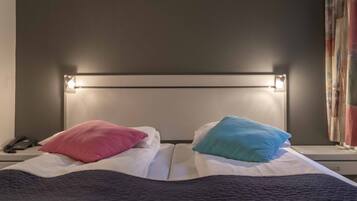 Una cama con cabecera, dos almohadas, un teléfono en la mesita de noche y una ventana con cortinas.