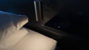 Una cama con colchón blanco y cabecera con panel de control y un objeto cilíndrico, posiblemente un calefactor o purificador de aire.