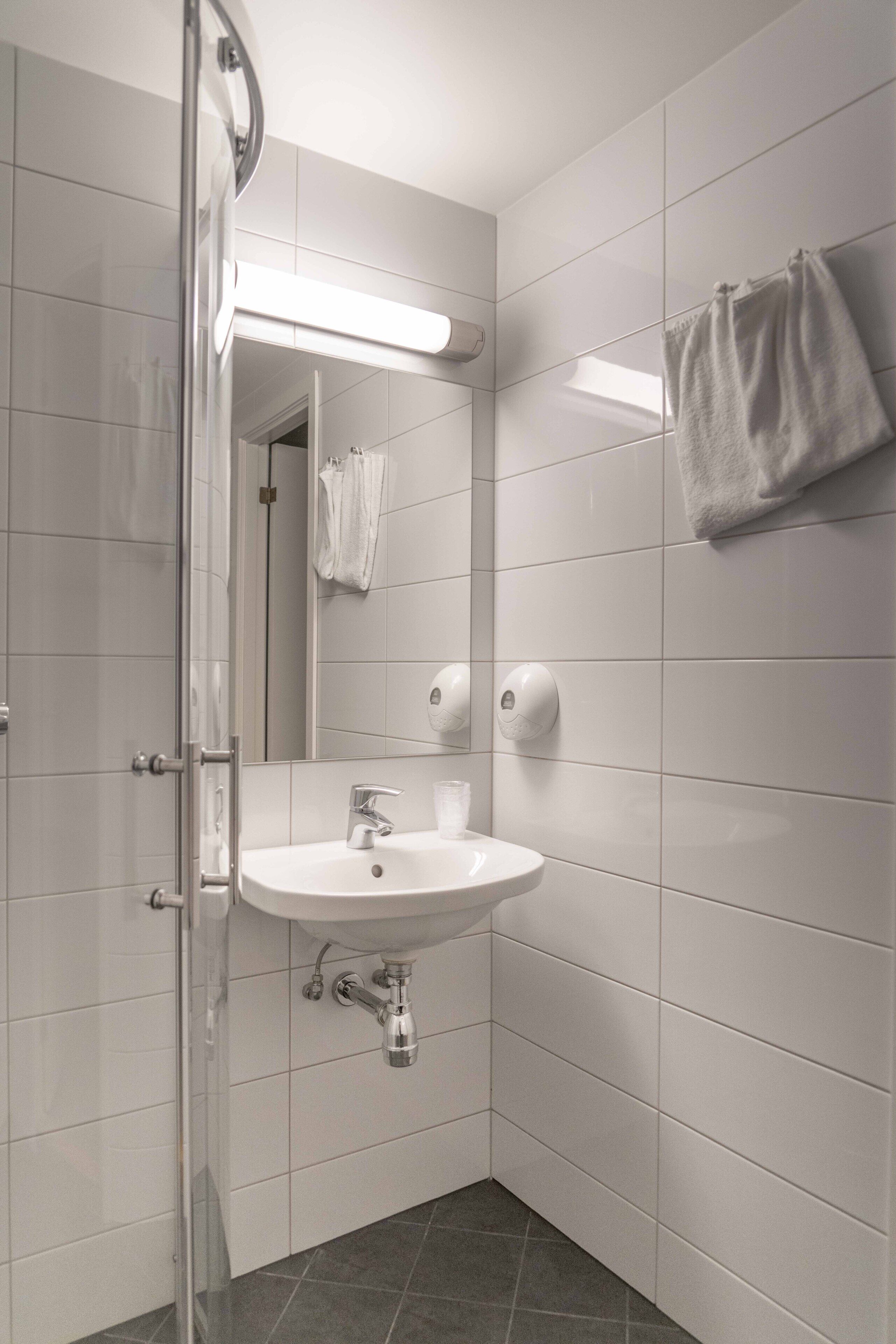 Ein modernes Badezimmer mit einer Duschkabine aus Glas, einem weißen Waschbecken mit Spiegel darüber und einem Handtuch an der Wand.