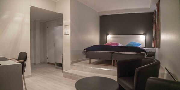 A modern hotel room with a bed, a desk, a chair, and a small table.