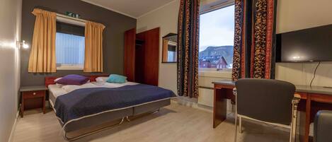 A hotel room with a bed, a desk, a chair, a TV, and a window with curtains.