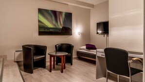 A modern hotel room with a large painting of the Northern Lights, a bed with a purple pillow, a desk with a computer, and two leather chairs. - Melbu Hotell  (Hadsel)