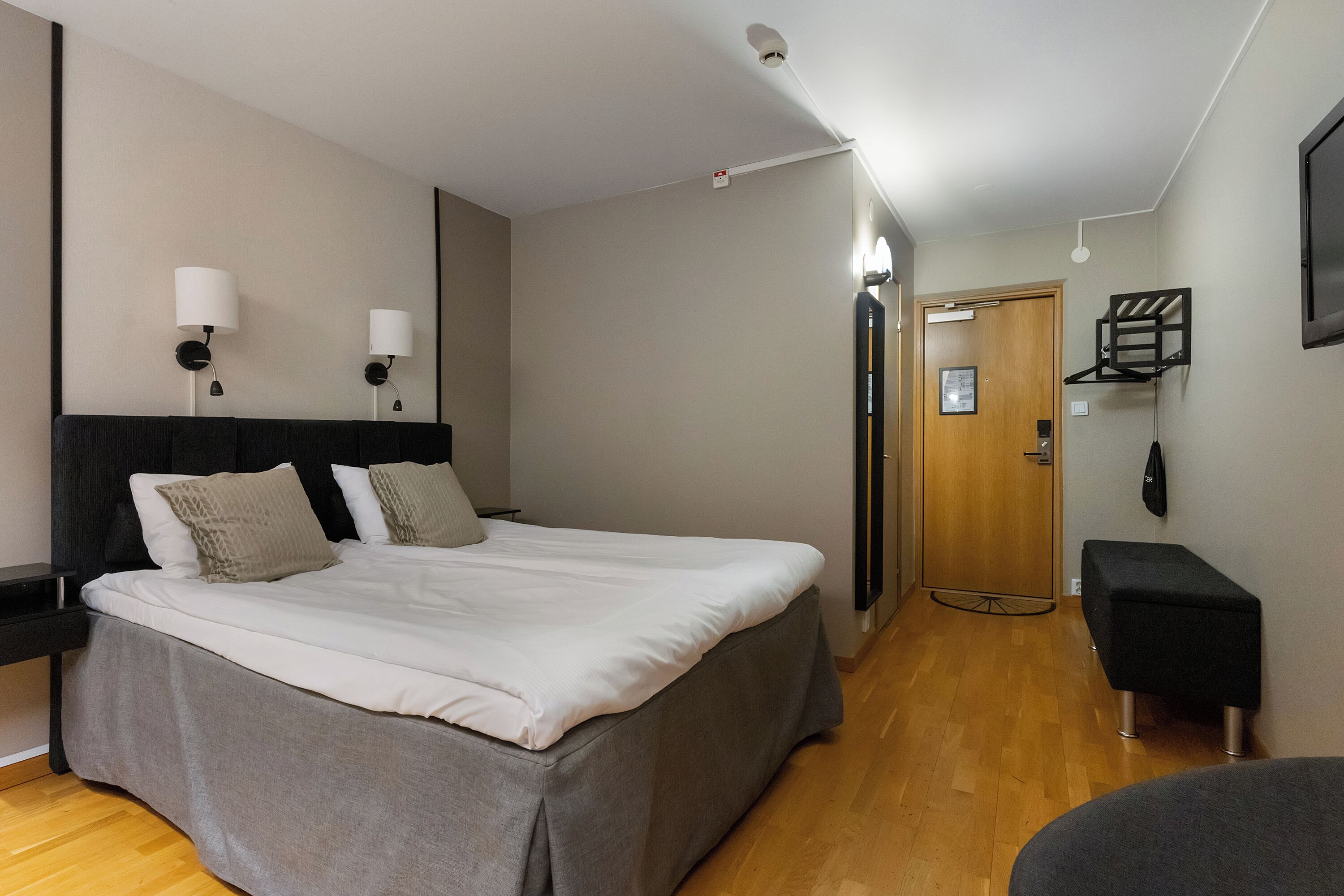 A modern hotel room with a large bed, bedside lamps, a wooden door, and a small seating area.