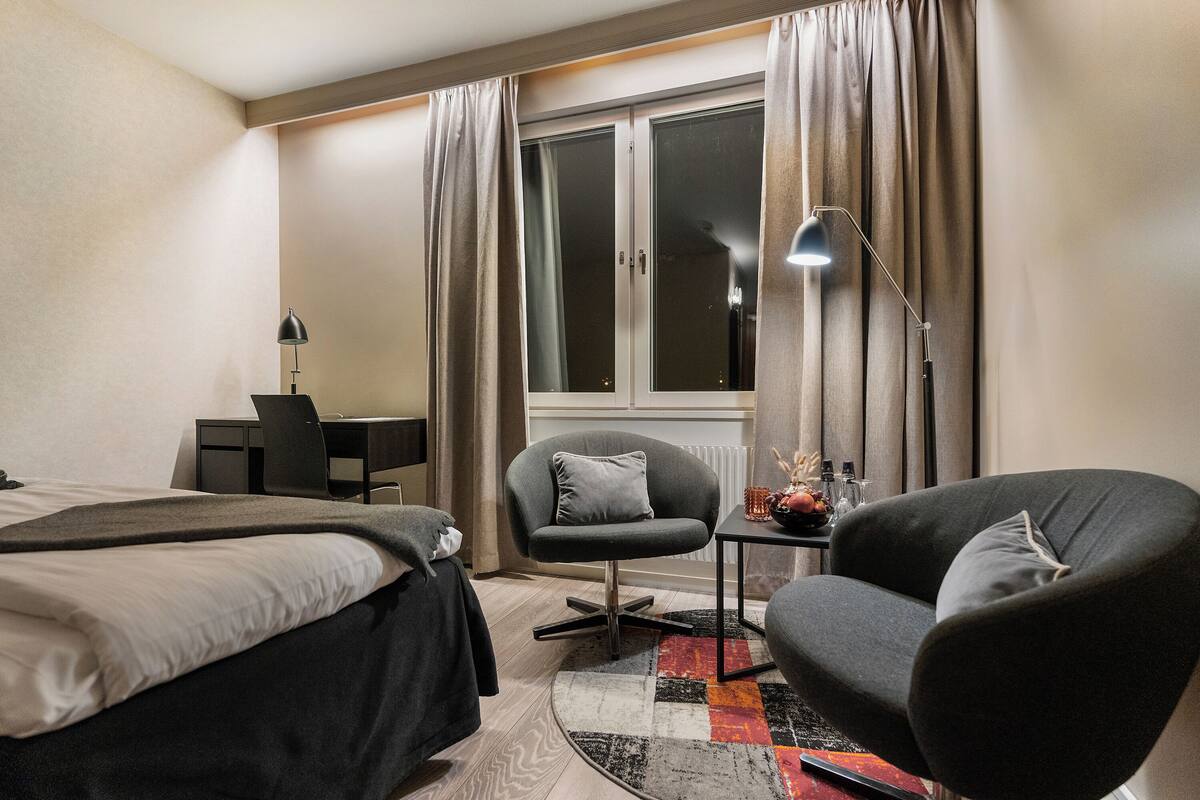 Una habitación de hotel con dos camas, un escritorio, una silla y un ventanal con cortinas.