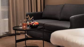 Una habitación de hotel moderna con un sofá de color gris oscuro, una mesita redonda con fruteros, vasos y botellas.
