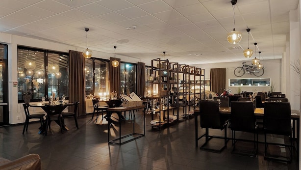 A spacious dining area with multiple tables and chairs, a large bookshelf, and a motorcycle on the wall. - Quality Hotel Vanersborg (Vanersborg)