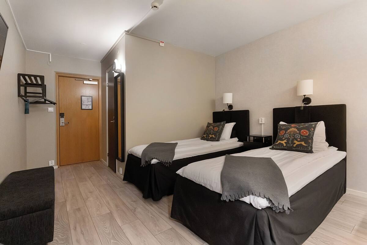 Habitación de hotel con dos camas, un pequeño rincón de descanso y una puerta que da a un baño.