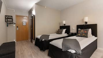 Quarto de hotel com duas camas, um espaço de estar pequeno e uma porta para o banheiro.