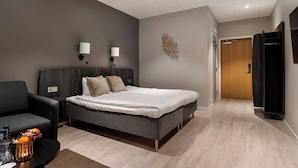 A modern hotel room with a large bed, a sofa, two wall-mounted lamps, and a decorative wall piece. - Quality Hotel Vanersborg (Vanersborg)