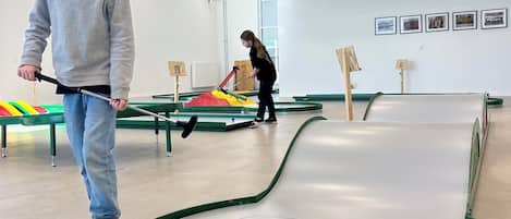 Una sala de billar con mesas verdes y blancas, una bola amarilla y una persona jugando.