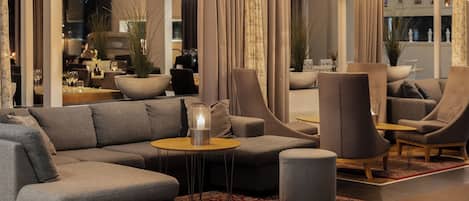 Ein modernes Wohnzimmer mit Ecksofa, Sesseln, einem kleinen runden Tisch und einer Stehlampe.