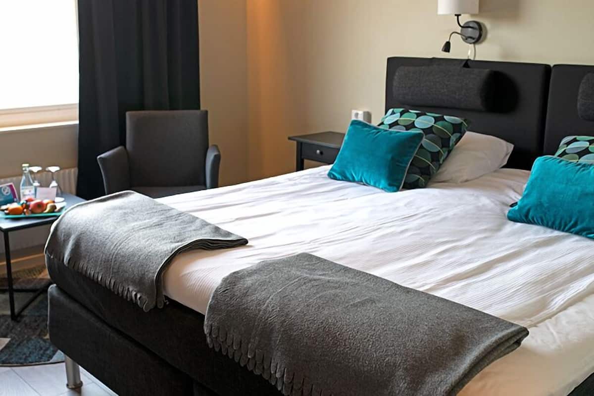 Habitación de hotel con cama, escritorio, computadora portátil, silla y ventana con cortinas.