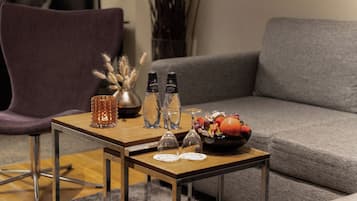 Un salon moderne avec un canapé gris, une table basse en bois sur laquelle se trouvent un vase, deux bouteilles et un saladier rempli de fruits.