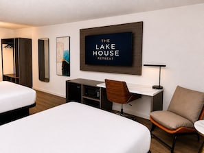A hotel room with two beds, a desk with a chair, a TV, and a mirror.