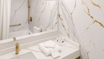 Un baño con pared de mármol, un espejo grande, un grifo dorado, un lavamanos y un perchero para toallas.