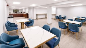 Un moderno salón de conferencias con mesas y sillas, una zona de cocina y un amplio ventanal.