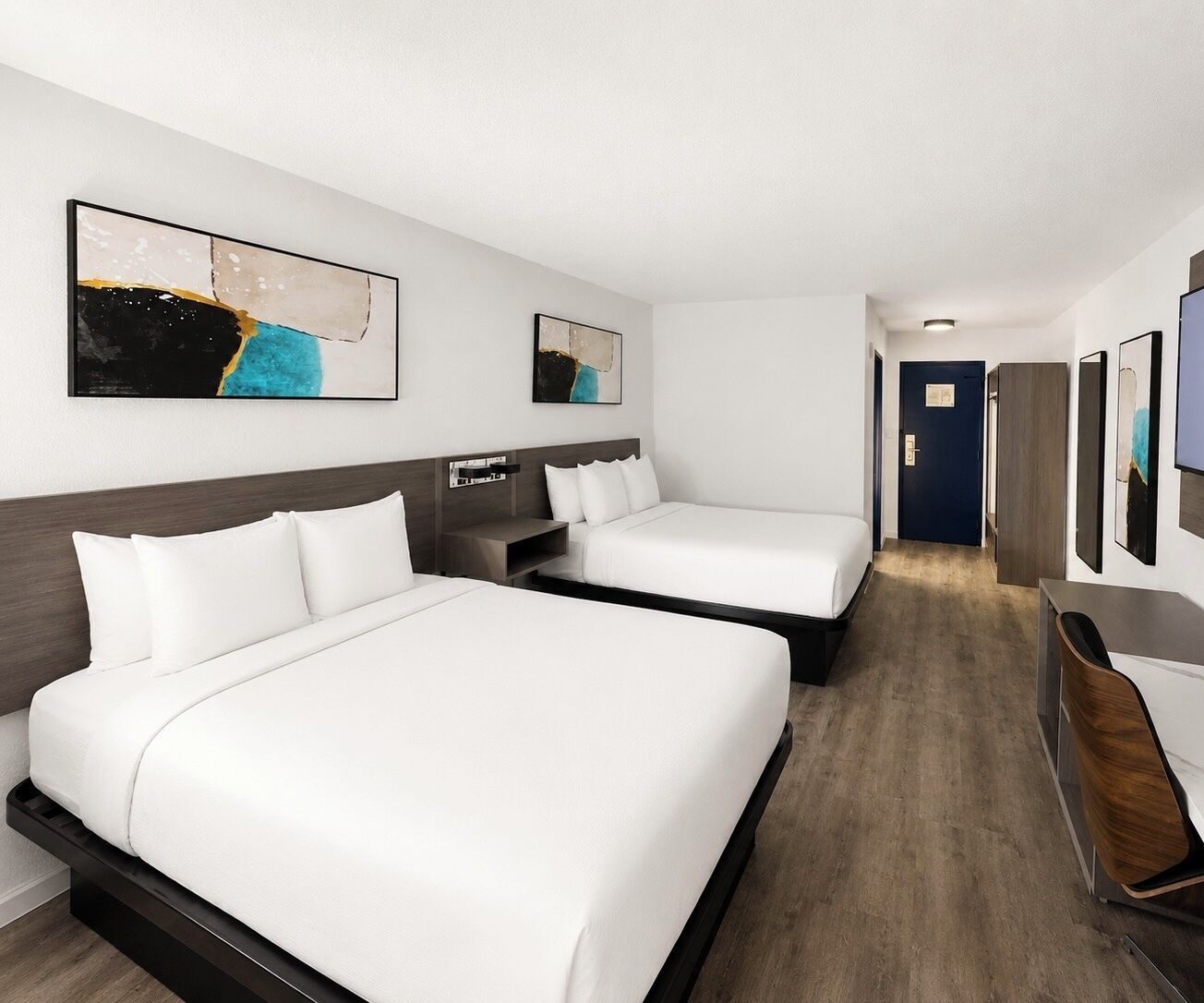 A hotel room with two beds, a desk, and artwork on the walls.