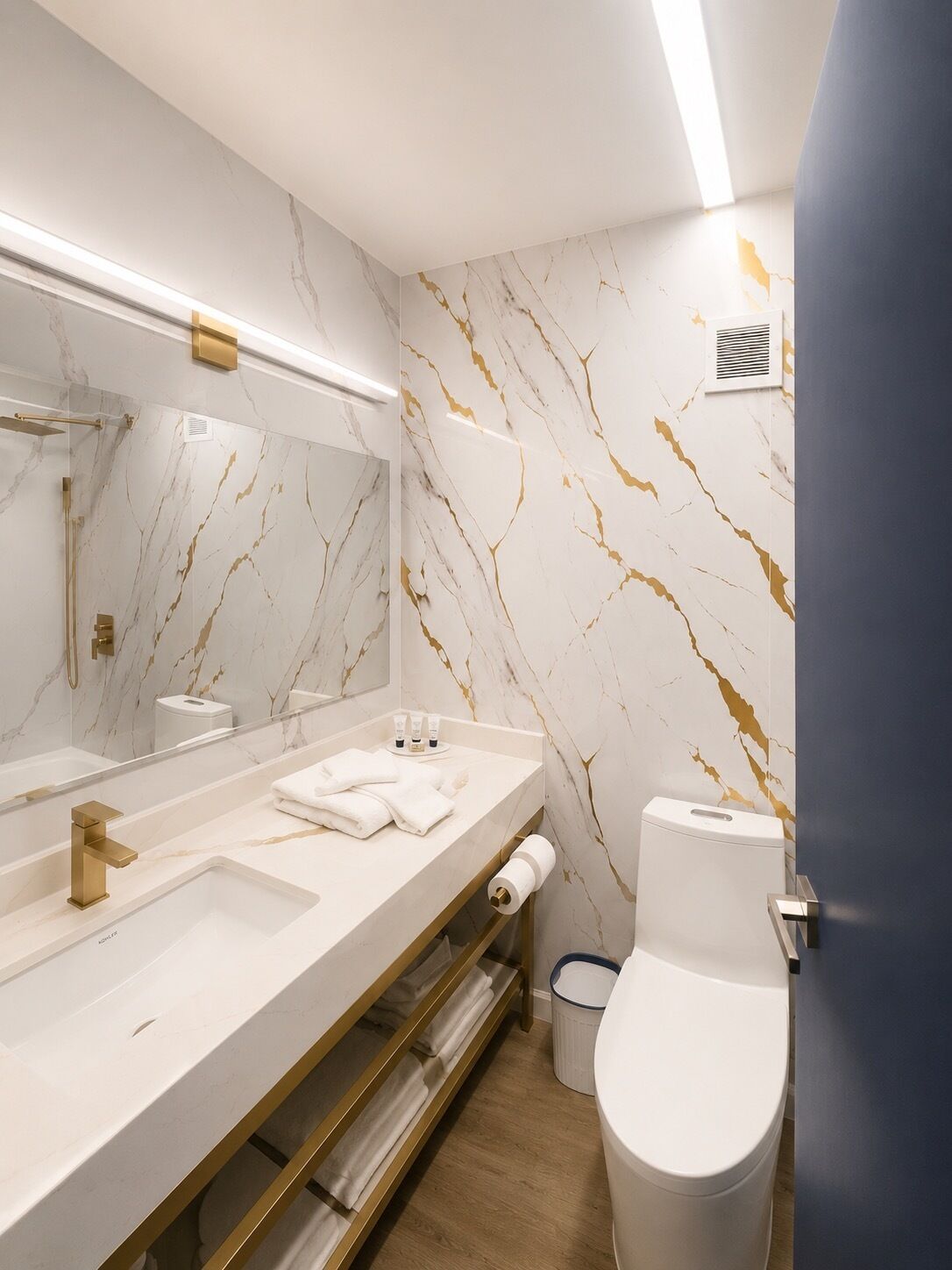 Une salle de bain moderne avec un pare-baignoire en marbre, un grand miroir, un robinet doré, des toilettes blanches et un porte-serviettes.