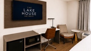 Habitación de hotel con televisor de pantalla plana, escritorio con silla, mesita de noche con lámpara, cama y ventana con cortinas.