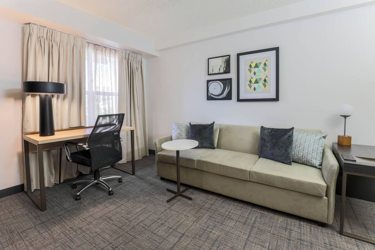 A hotel room with a desk, office chair, sofa, and a small round table.
