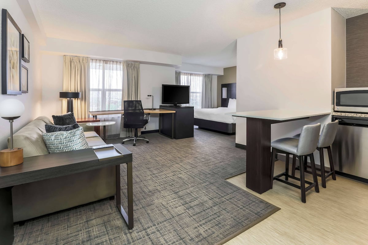 A hotel room with a bed, a desk, a TV, a sofa, and a dining area.