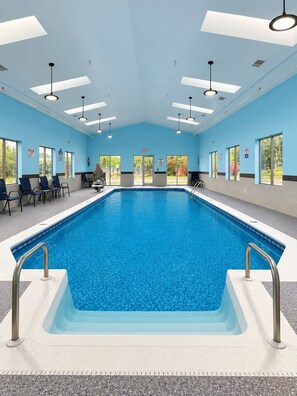 An indoor swimming pool with clear blue water, surrounded by chairs and a seating area.