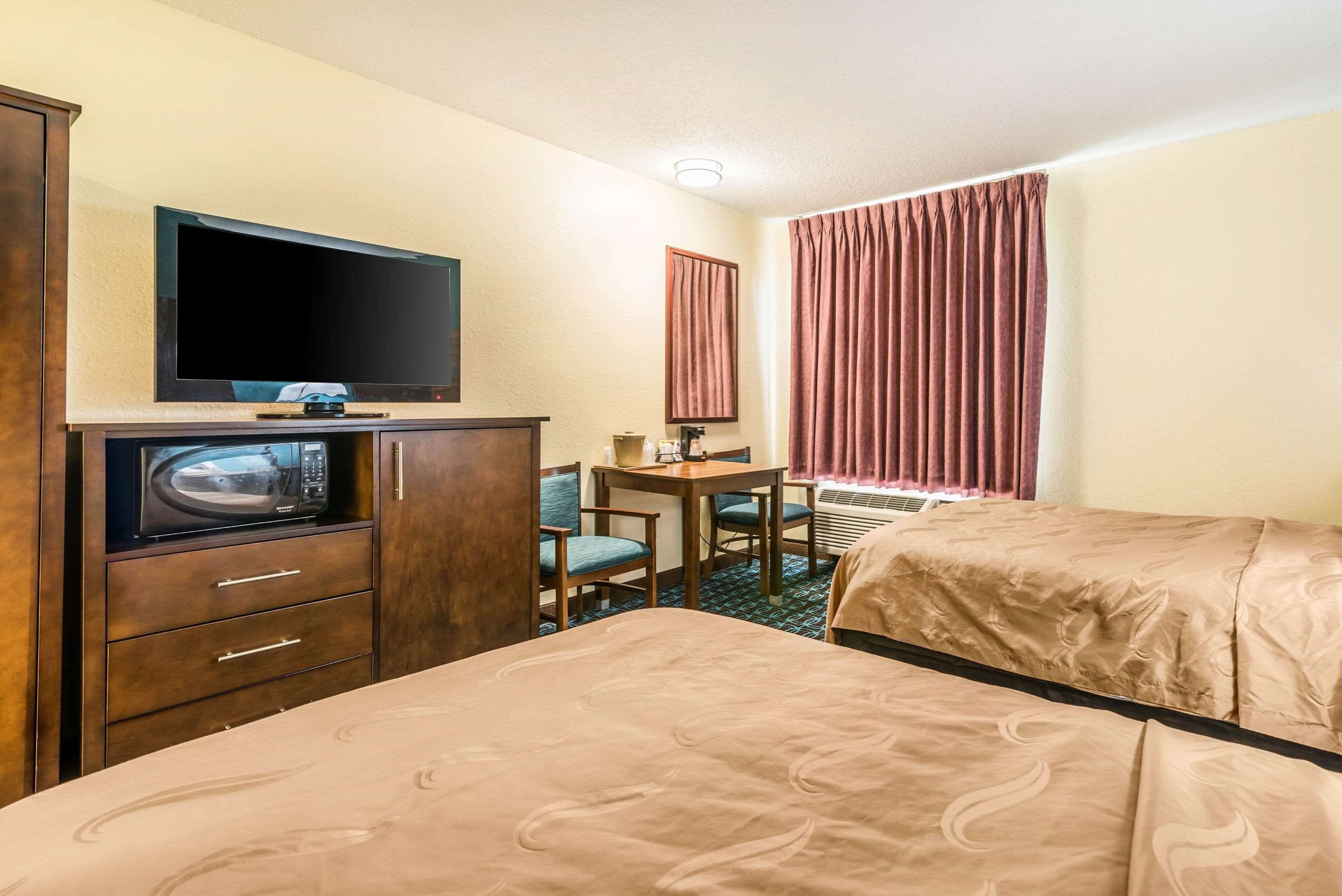 Una habitación de hotel con una cama, un escritorio con una silla, un televisor y un microondas.