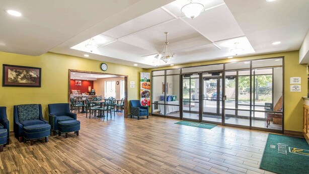 A lobby with wooden flooring, blue chairs, a reception desk, and a glass door leading outside. - Quality Inn Loudon-Concord (Loudon)