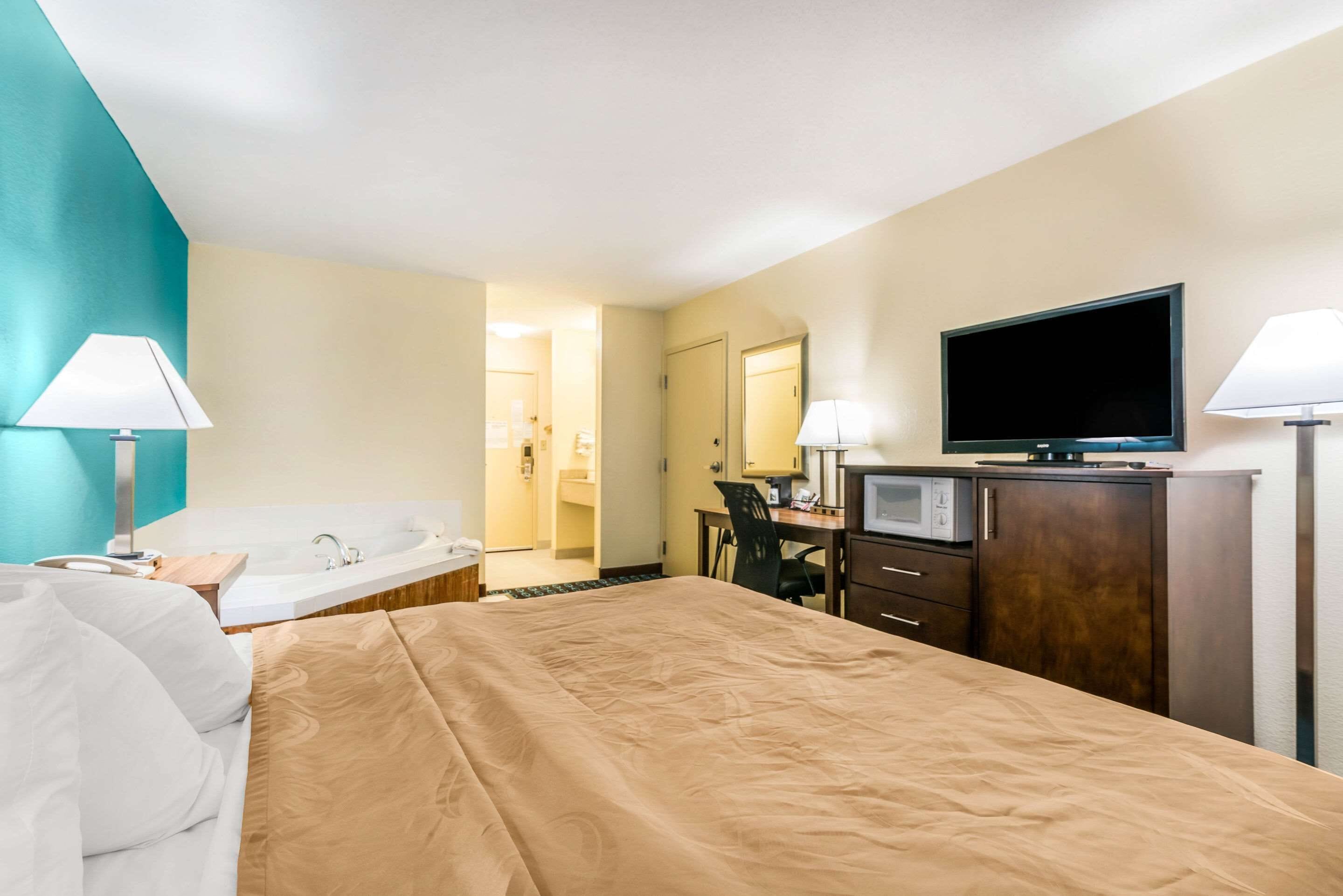 Une chambre d’hôtel avec un lit, un bureau, une télévision, un four à micro-ondes et une salle de bain visible à travers une porte ouverte.