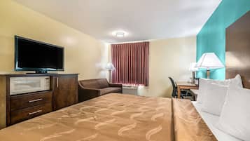 Una habitación de hotel con cama, escritorio, silla, televisión y microondas.