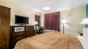 Ett hotellrum med en säng, en tv, ett skrivbord med en lampa, en mikrovågsugn och en garderob.