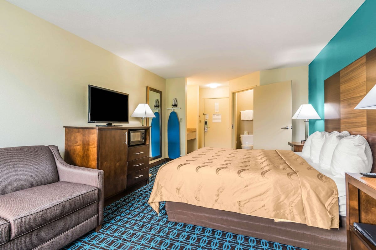 A hotel room with a bed, a sofa, a television, a dresser, and a bathroom visible through an open door.
