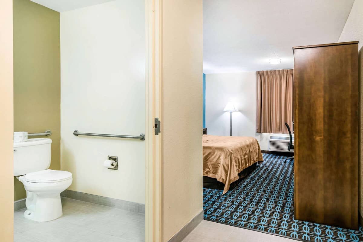 A hotel room with a toilet, a bed with a brown bedspread, a wooden wardrobe, and a patterned floor.