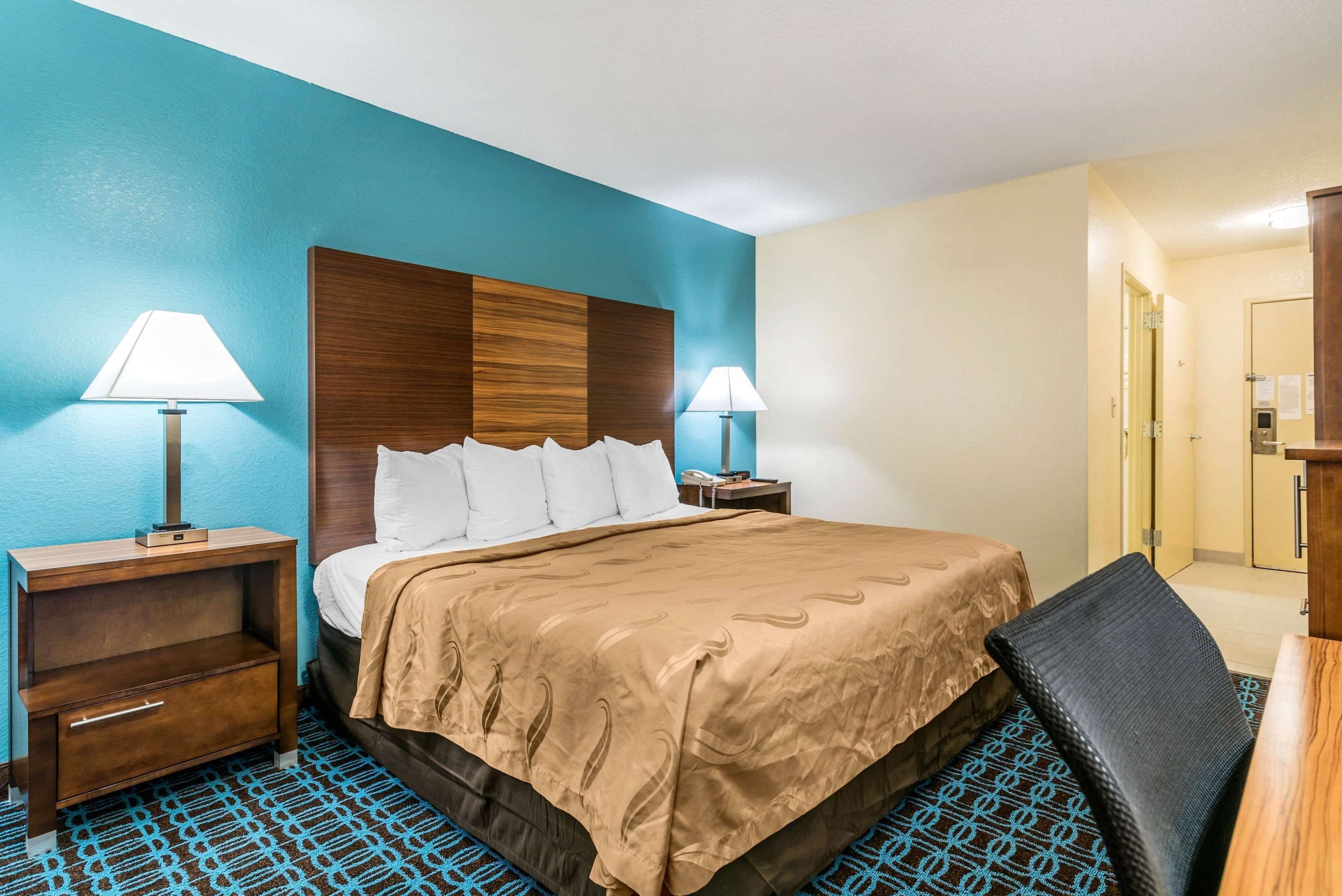 A hotel room with a bed, two bedside tables with lamps, a chair, and a desk.