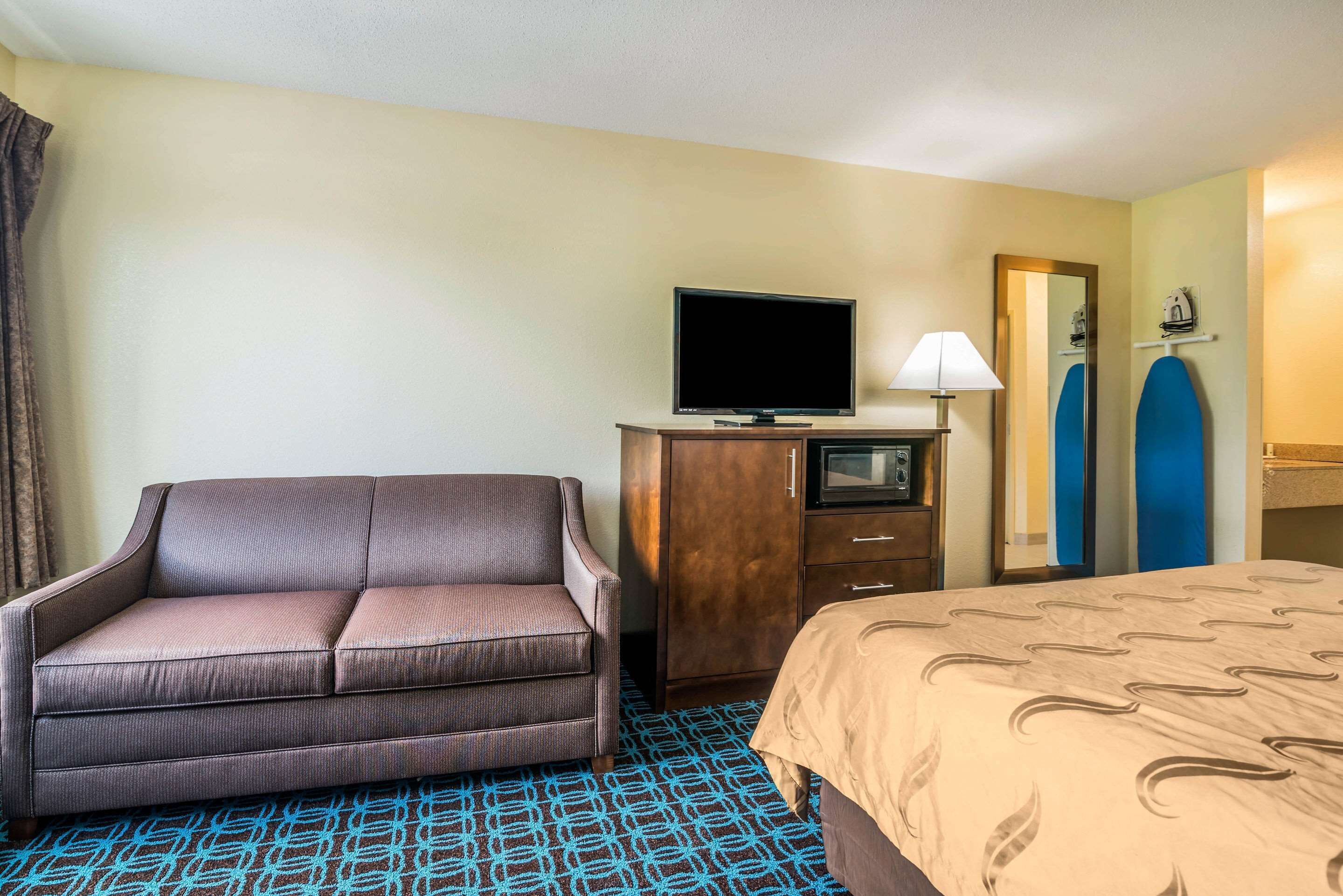 Habitación de hotel con sofá, cama, televisor, escritorio y espejo.
