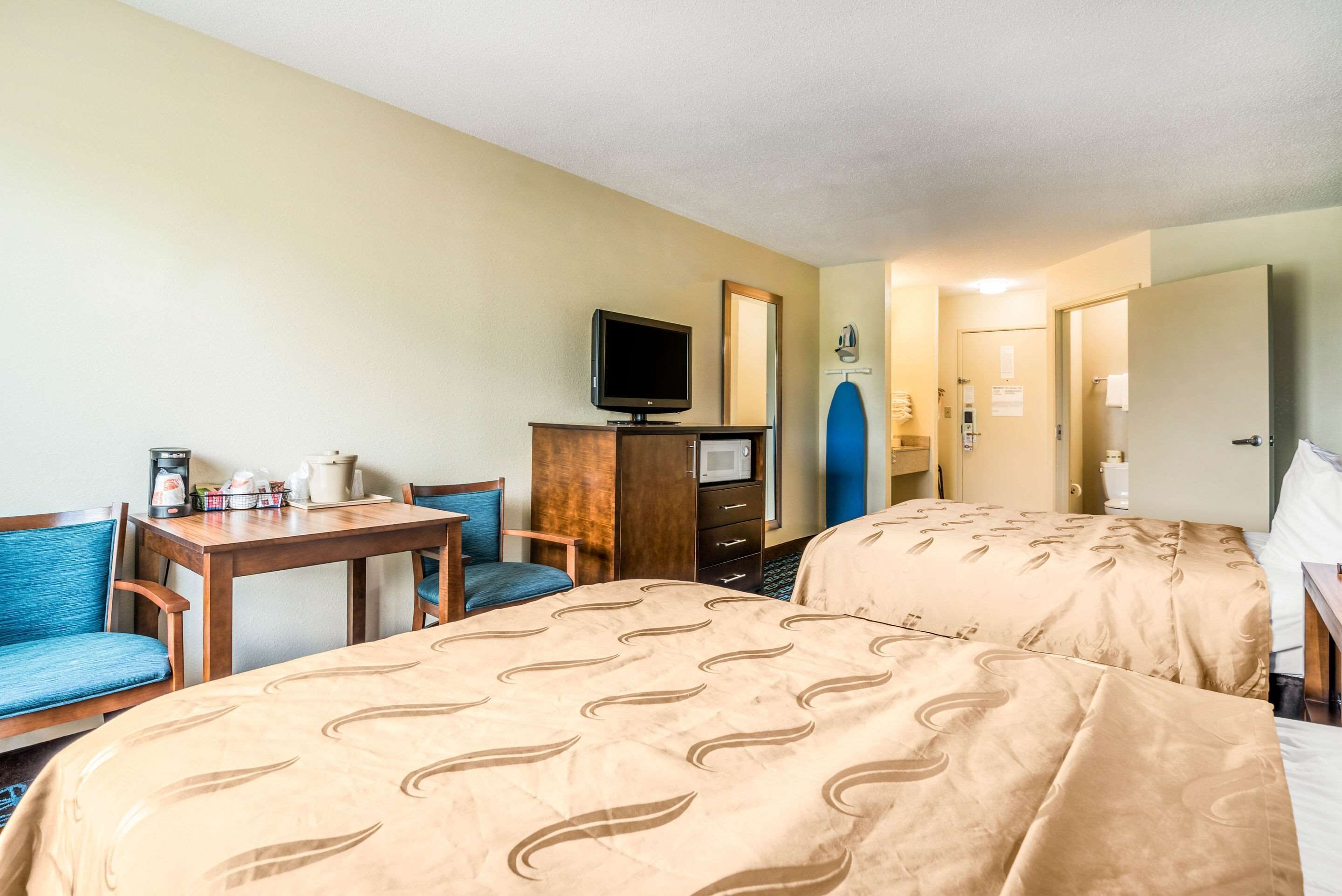 Ein Hotelzimmer mit zwei Betten, einem Fernseher, einem Schreibtisch mit Stuhl und einem kleinen Tisch mit Kaffeemaschine.