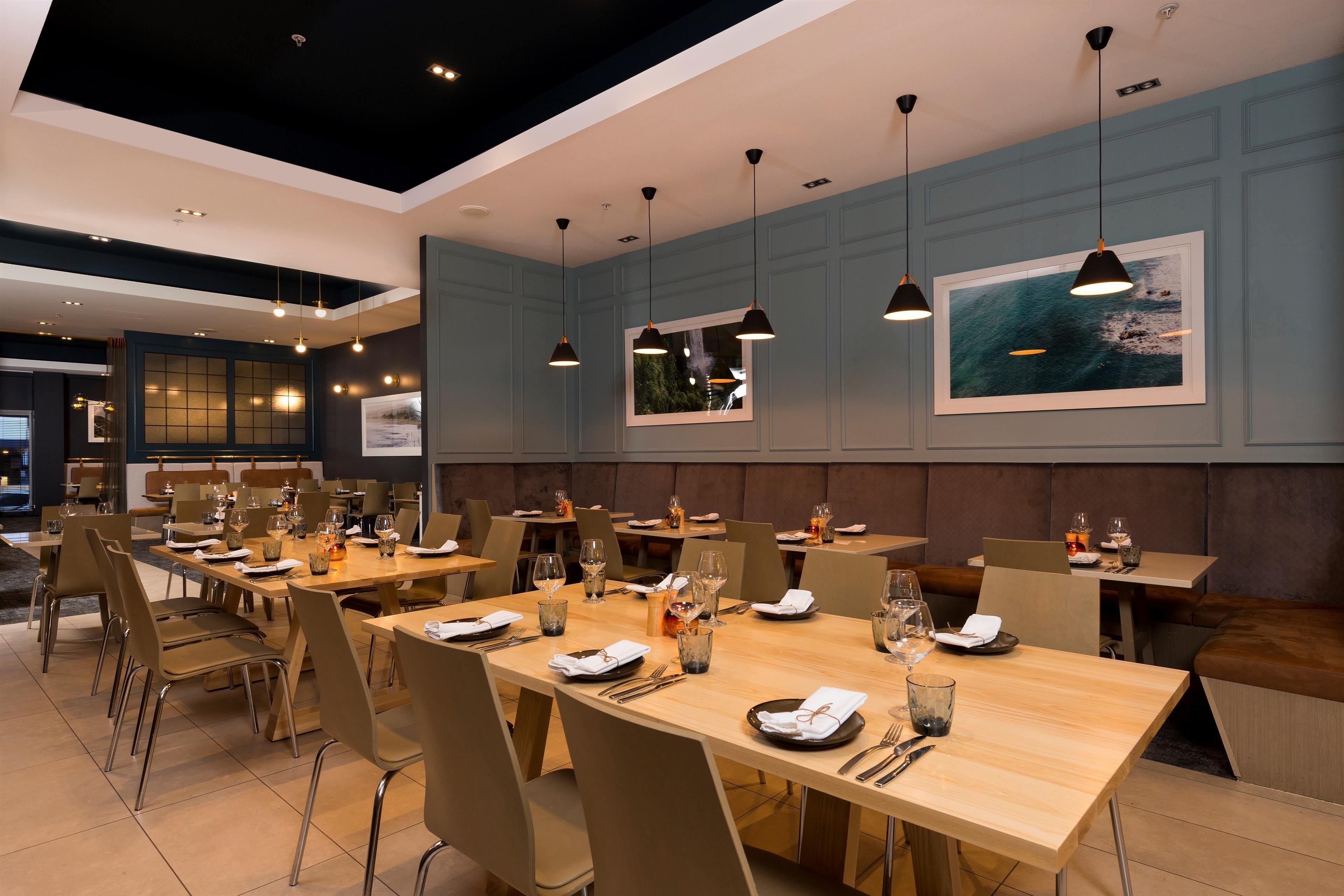 Ein modernes Restaurant mit langen Holztischen, beigen Stühlen und Pendelleuchten.