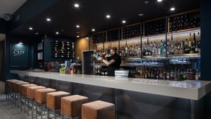 A bar area with a bartender, a long counter with stools, and shelves stocked with bottles and glasses. - Rydges Auckland (Auckland)